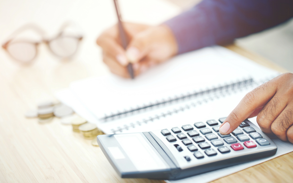 A business owner with a pen, paper and calculator going over his new marketing budget plan. 