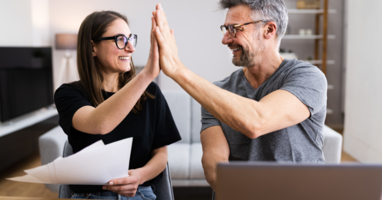 Two people are smiling and high-fiving each other because they are getting so many marketing tax write-offs for their business.