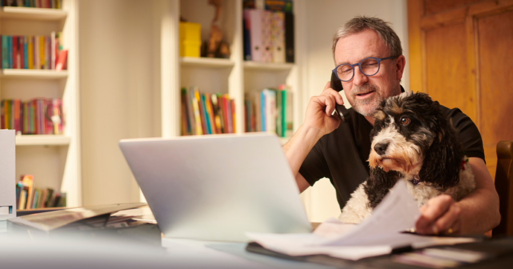 A man and his dog sit at a laptop and speak on the phone while conducting research to find a digital marketing agency for his business.